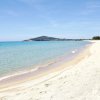 Spiaggia sabbiosa con mare turchese e colline in lontananza.
