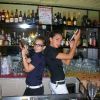 Due baristi al bancone con shaker, circondati da bottiglie.