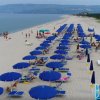 Spiaggia con ombrelloni blu e mare calmo.