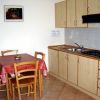 Cucina con mobili in legno chiaro, tavolo rettangolare coperto da tovaglia rossa, quattro sedie.
