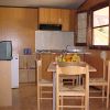Cucina con tavolo rettangolare, quattro sedie, frigorifero piccolo, e mensole. Finestra aperta.