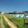 Un prato verde conduce a una piscina con sdraio. Edifici bassi in lontananza sotto un cielo blu.