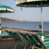 Ombrelloni e sdraio verdi su una spiaggia, con mare e costa sullo sfondo.