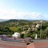 Panorama di colline verdi con cielo azzurro e alcune case in lontananza.