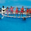 Persone in piedi su piattaforme in una piscina, alcune indossano costumi a tema carte da gioco.