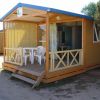 Chalet in legno con veranda e sedie bianche su una terrazza.