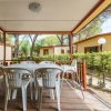 Veranda con tavolo e sedie bianche, circondata da bungalow e natura.